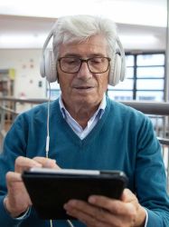 Ein Senior mit Kopfhörer bedient ein Tablet