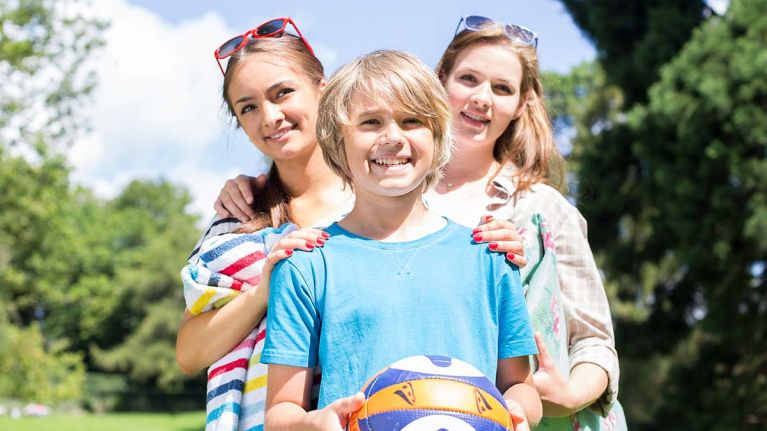 Zwei Mädchen stehen hinter einem Jungen, der einen Ball hält