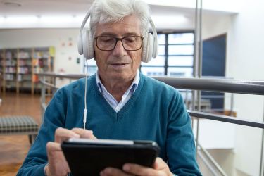 Ein Senior mit Kopfhörer bedient ein Tablet