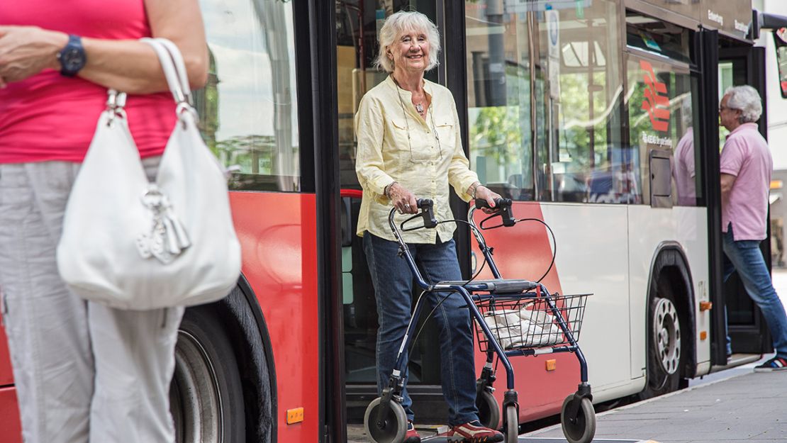 Alte Frau mit Rollator steigt aus einem Bus aus.